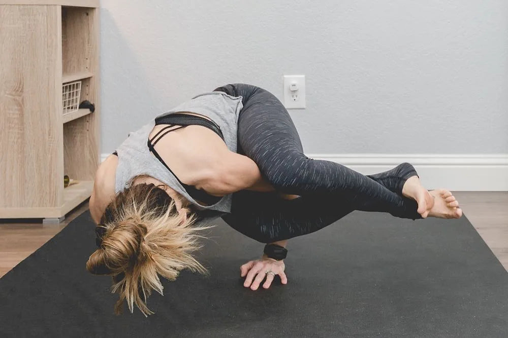 Woman balancing in an arm-balance yoga pose on a black mat over a wood floor