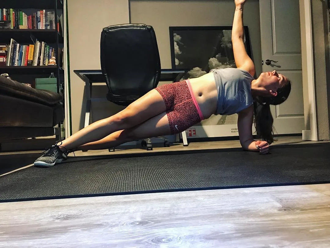 Woman in a side plank in sneakers on a large black mat in her home office