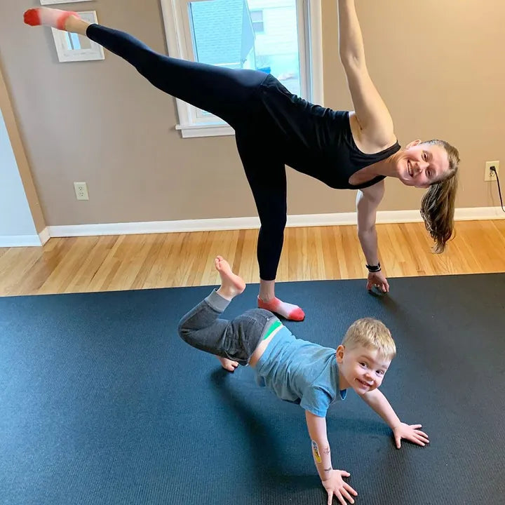 Mom in a half-moon balance on a large mat while her son crawls beside her