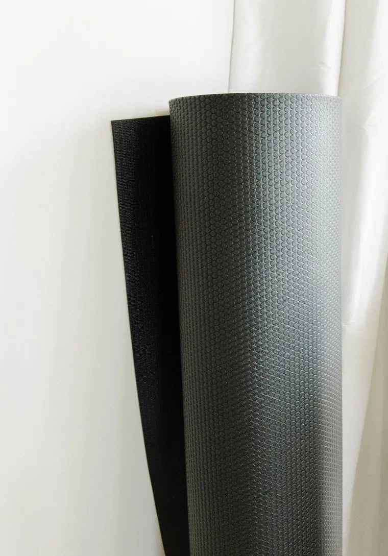 A rolled black mat standing against a white curtain
