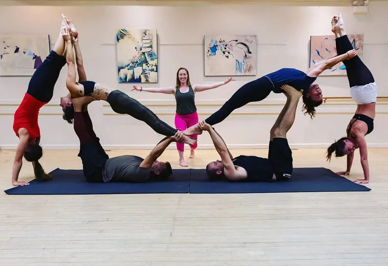 A group doing partner acrobatic yoga on a long mat in a dance studio