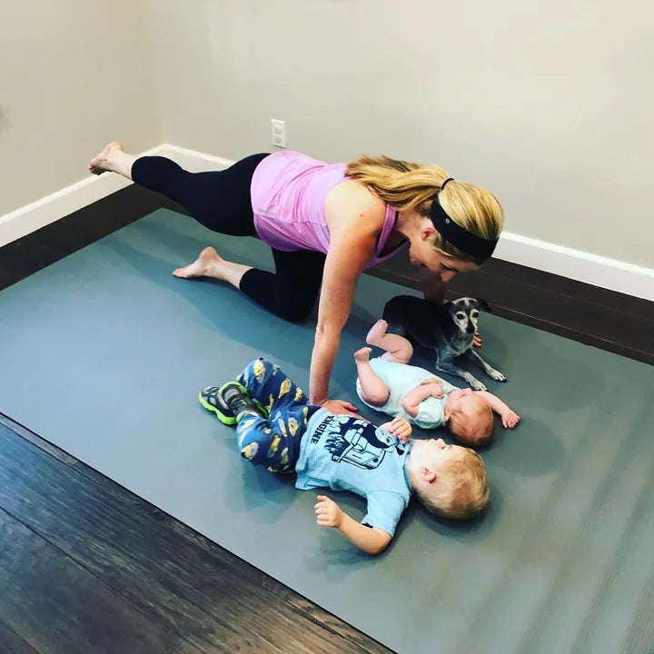 Mom in a plank over her two toddlers lying on a large mat